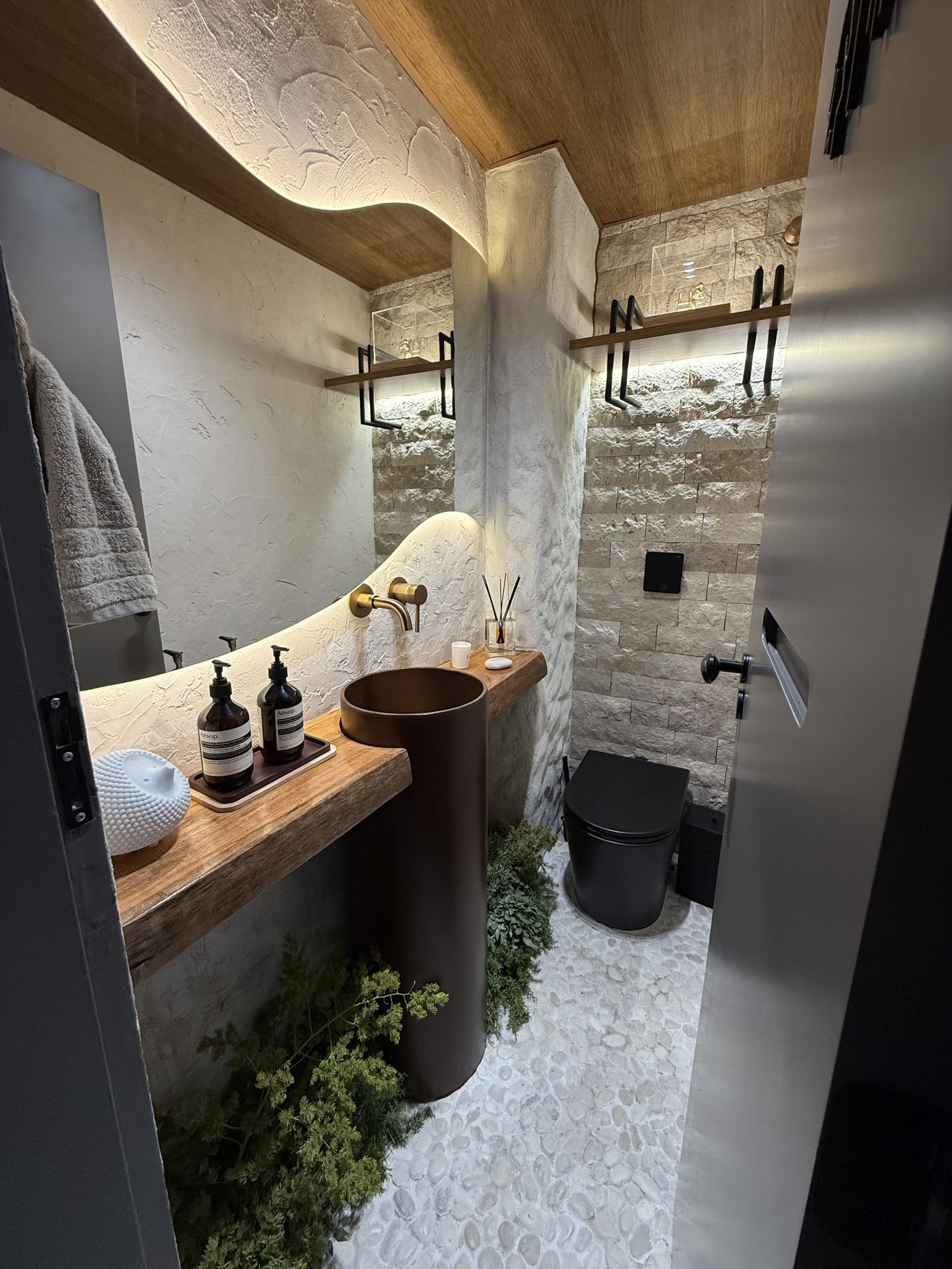 Lavabo com bancada curva, pedra e plantas
